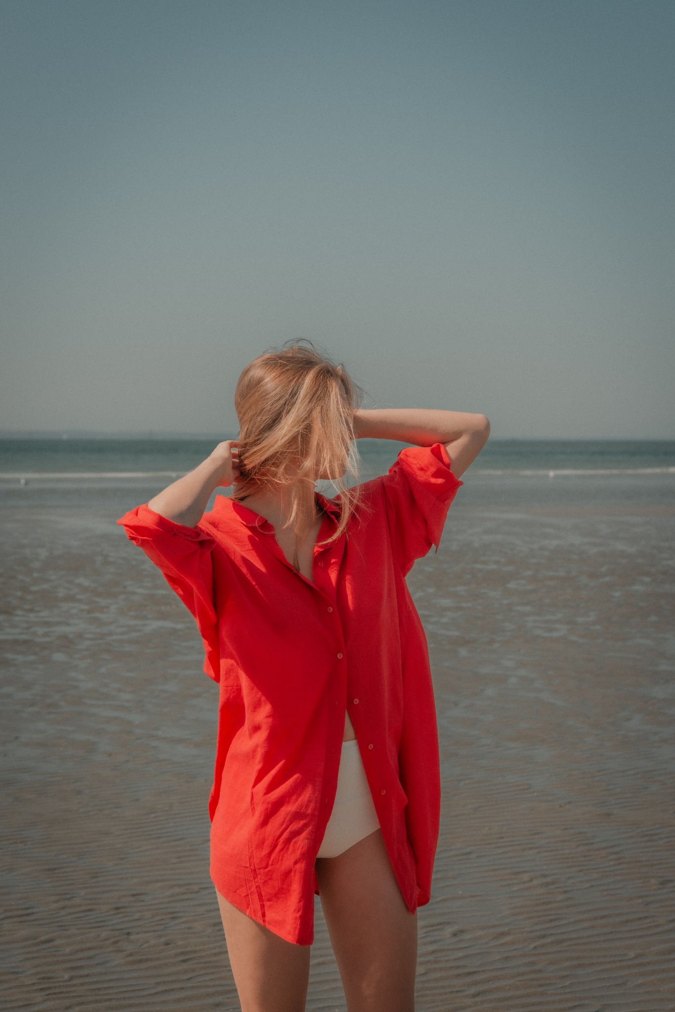 Model in red shirt standing on the beach for an editorial fashion story by Lucy Rappolt